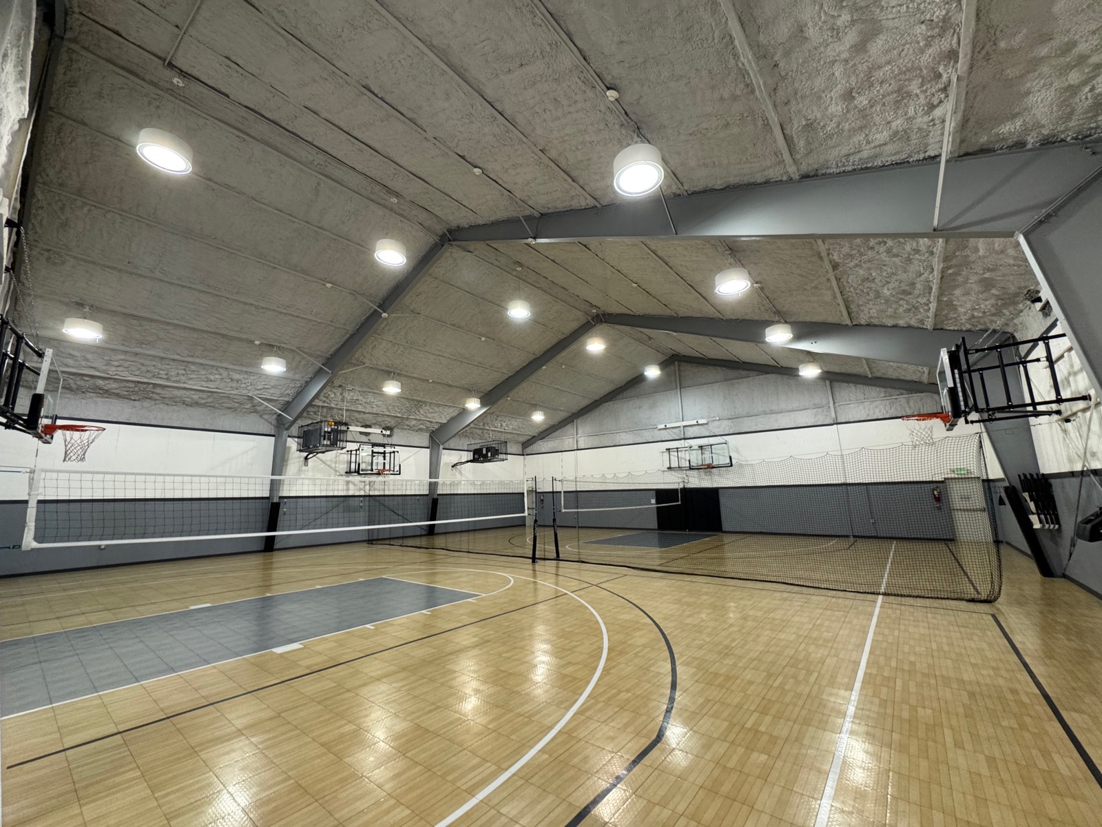 Court with two volleyball nets deployed across the floor and hoops folded against the wall